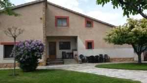 una casa con ventanas rojas y un patio con flores púrpuras en Casa Rural Las Tuyas en Segovia en Palazuelos de Eresma