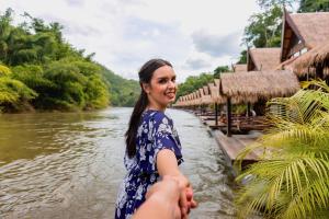 a woman holding the hand of a person next to a river at The Float House River Kwai in Sai Yok +27 photos