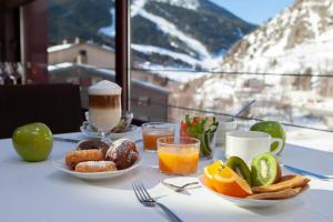 - une table avec des assiettes de produits pour le petit-déjeuner et des boissons dans l'établissement Wuau! Hotel Galanthus & Spa, à Soldeu