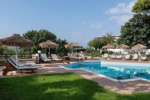 a pool with chairs and umbrellas next to a yard at Alianthos Suites in Tersanas