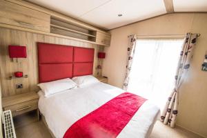 een slaapkamer met een bed met een rood hoofdeinde en een raam bij River Lodge Platinum Plus Holiday Home with River Views, Free Wifi & Netflix in Camber
