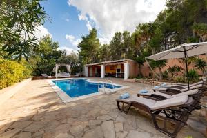 a pool with lounge chairs and an umbrella next to a house at Villa Mercedes in Cala Llonga
