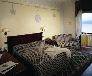 a bedroom with a bed and a chair and a table at Hotel Lugana Parco Al Lago in Sirmione