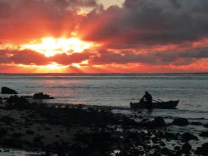 a man sitting in a boat on the beach at sunset at The Sands Hotel Hokianga in Opononi