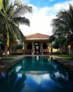 a swimming pool in front of a house with palm trees at Villa Setha Wadi in Kalpitiya