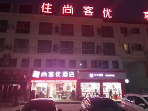 a building with neon signs and cars parked in front of it at Thank Inn Plus Hotel Jiangsu Taizhou Gaogang Port Middle School in Taizhou