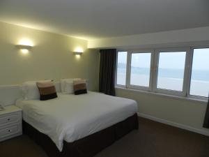 una camera da letto con letto, lenzuola bianche e finestre di Beau Rivage a St Brelade