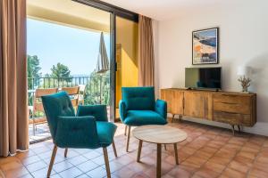 a living room with chairs and a television and a balcony at La Résidence du Bailli in Rayol-Canadel-sur-Mer