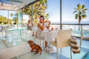 ディアーノ・マリーナにあるHotel Caravelle Thalasso & Wellnessの犬と一緒にレストランのテーブルに座っている女性