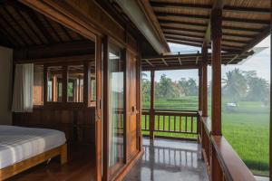 a bedroom with a bed and a view of a field at Benisari Batik Garden Cottage in Ubud