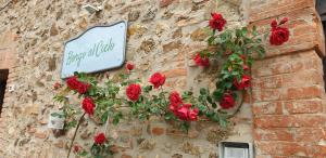 a sign on the side of a brick wall with red roses at Borgo al Cielo - Albergo Diffuso in Suvereto