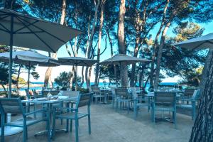 ein Restaurant im Freien mit Tischen, Stühlen und Sonnenschirmen in der Unterkunft Iberostar Pinos Park in Font de Sa Cala