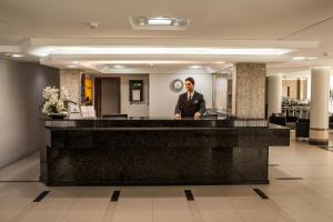 a man standing behind a counter in a lobby at Hamburgo Palace Hotel in Balneário Camboriú