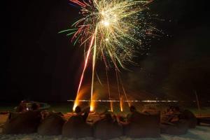 un grupo de personas sentadas en la playa viendo fuegos artificiales en Sunset Beach Bungalow en Gili Meno