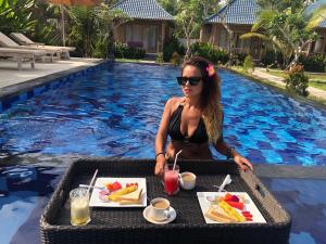 a woman sitting at a table with a meal by a pool at Kayuna Villa in Nusa Penida