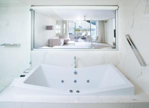Sofitel Noosa Pacific Resort في نوسا هيدز: حمام أبيض مع مرآة كبيرة وحوض استحمام