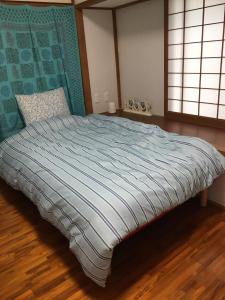 a bedroom with a bed with a blue comforter and two windows at Kami House in Amami