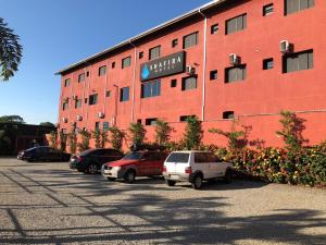 ein großes rotes Gebäude mit Autos auf einem Parkplatz in der Unterkunft Shafira Hotel in Limeira