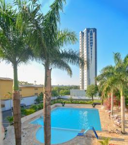 a swimming pool with palm trees and a building at Iguassu Flats Hotel in Foz do Iguaçu