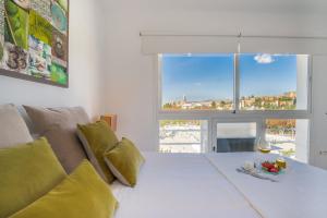 Una cama blanca con una copa de vino y una ventana en LU&CIA Málaga Skyline, en Málaga