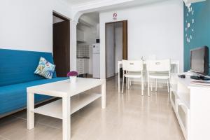 8202 - Wifi Costa Calma Bungalow في كوستا كالما: غرفة معيشة مع أريكة زرقاء وطاولات وكراسي بيضاء