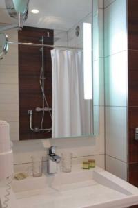 La salle de bains est pourvue d'une douche et d'un lavabo avec un miroir. dans l'établissement Hôtel Panorama, à Munster