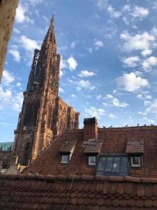 un bâtiment avec une tour d'horloge derrière un toit dans l'établissement Carpe Diem Home - Au pied de la Cathédrale, à Strasbourg