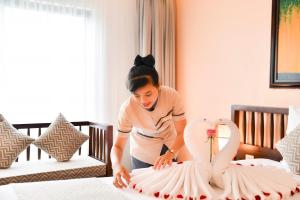 a woman making a swan decoration on a bed at Fivitel Hoi An Hotel in Hoi An