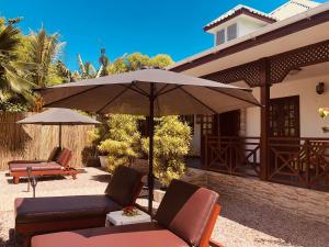 eine Terrasse mit Stühlen und einem Sonnenschirm vor einem Haus in der Unterkunft Sunset Cove Villa in Grand'Anse Praslin