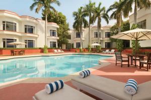 a resort pool with chairs and tables and palm trees at Ramada Khajuraho in Khajurāho