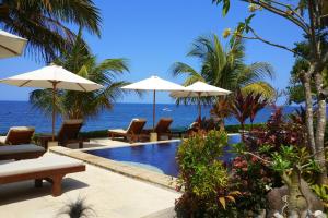a pool with chairs and umbrellas next to the ocean at Alam Mimpi Bali in Tejakula