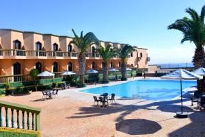 a resort with a swimming pool with palm trees and chairs at Hôtel Atlantique Panorama in Safi