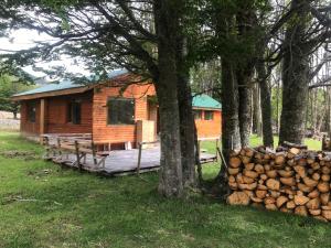 a log cabin in the woods with a pile of logs at Cabaña Lago Largo in Coihaique