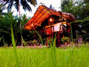 a small house with a thatched roof in a field at Aliya Riverside & Safari Resort in Udawalawe