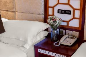 a bed with a vase of flowers and a phone on a table at Floral Hotel · Shangri-la Blue Sky in Shangri-La
