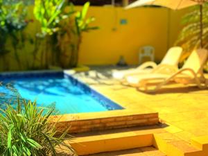 a swimming pool in a backyard with chairs and an umbrella at Pousada Costeira da Barra in Maragogi