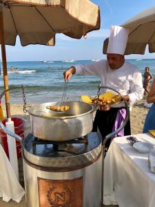 a man cooking food in a pot on the beach at Grand Hotel Il Ninfeo in Gaeta
