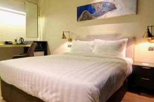 a bedroom with a white bed with a desk and a chair at Le Embassy Hotel Georgetown in George Town