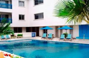 a swimming pool in front of a hotel with chairs and umbrellas at Napa Blue Apartment, XXL Pool,in Hearth of Ayia Napa in Ayia Napa