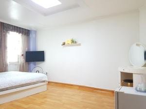 a white bedroom with a bed and a wooden floor at Nice View Guesthouse in Seogwipo