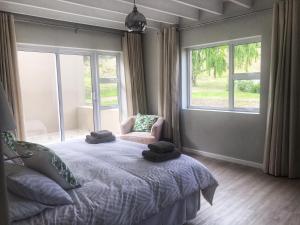 a bedroom with a bed and a chair and windows at The Suites at Waterryk Eco Guest Farm in Stilbaai