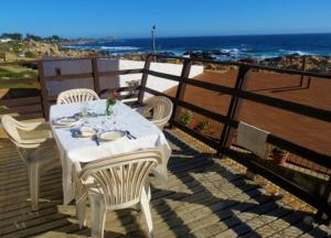 uma mesa branca e cadeiras num deque com o oceano em El Rincon de Las Pleyades em El Quisco