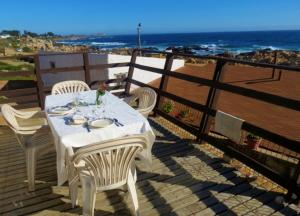 a white table and chairs on a deck with the ocean at El Rincon de Las Pleyades in El Quisco