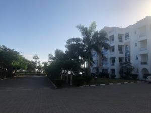 eine Straße vor einem weißen Gebäude mit Palmen in der Unterkunft Almasi Oceanfront Nyali in Mombasa