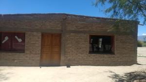 a small brick building with a wooden door and windows at Camping agreste El Algarrobo de Quilmes in Amaicha del Valle