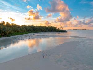 zwei Menschen, die bei Sonnenuntergang am Strand spazieren gehen in der Unterkunft Rahaa Resort Maldives in Laamu Atoll