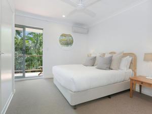 a white bedroom with a white bed and a window at Byron Beachside 8 in Byron Bay +8 photos