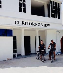 dos personas en bicicleta delante de un edificio en Ci-Ritorno View, en Maafushi