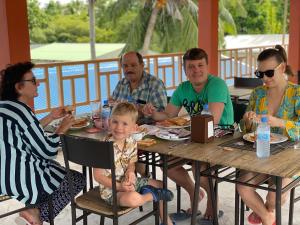 Eine Gruppe von Menschen, die an einem Tisch sitzen und Essen essen. in der Unterkunft Thoddoo White Sand Inn in Thoddoo-Atoll