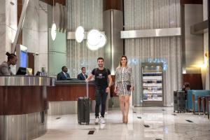 a man and woman walking through an airport with their luggage at Rose Rayhaan by Rotana - Dubai in Dubai